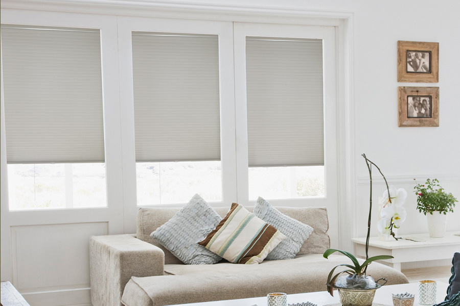 Cellular shades are energy-efficient for your living spaces. Light gray cellular shades on three separate windows in large light wood and beige colored living room.